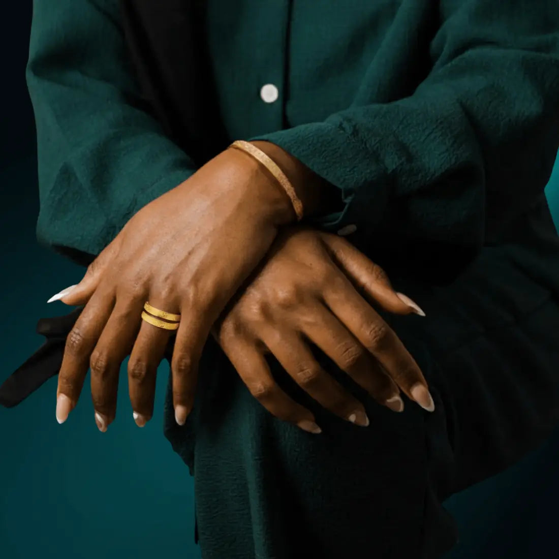 Crossed hands over a green sleeve wearing the gold-plated NUUR Ayatul Kursi Bracelet and ring