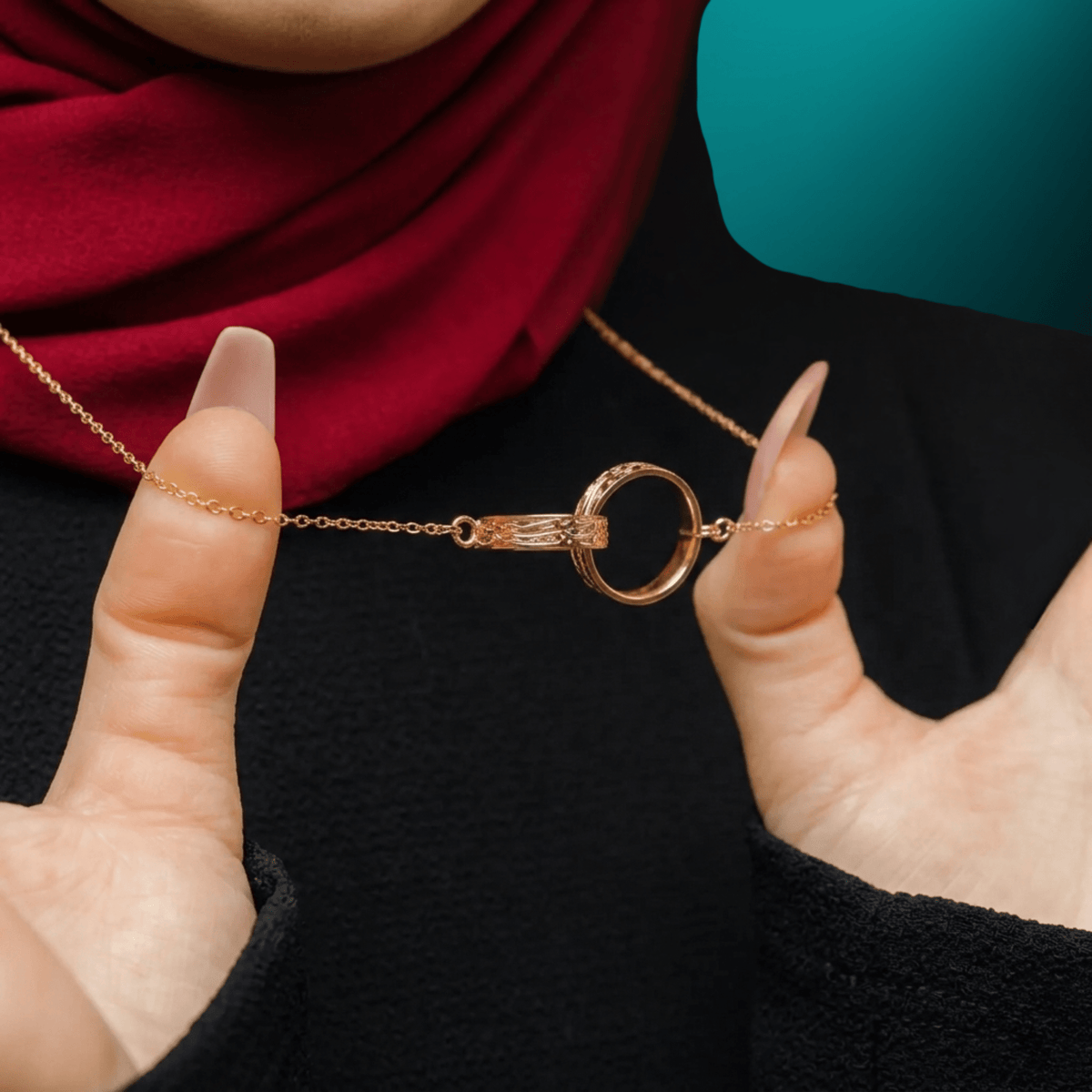 Close-up of the NUUR Sanad necklace, two interlocking gold rings held between fingers