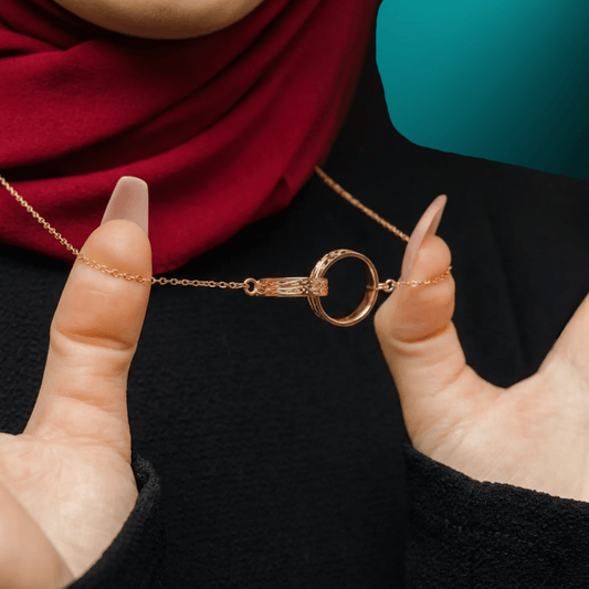 Close-up of the NUUR Sanad necklace, two interlocking gold rings held between fingers