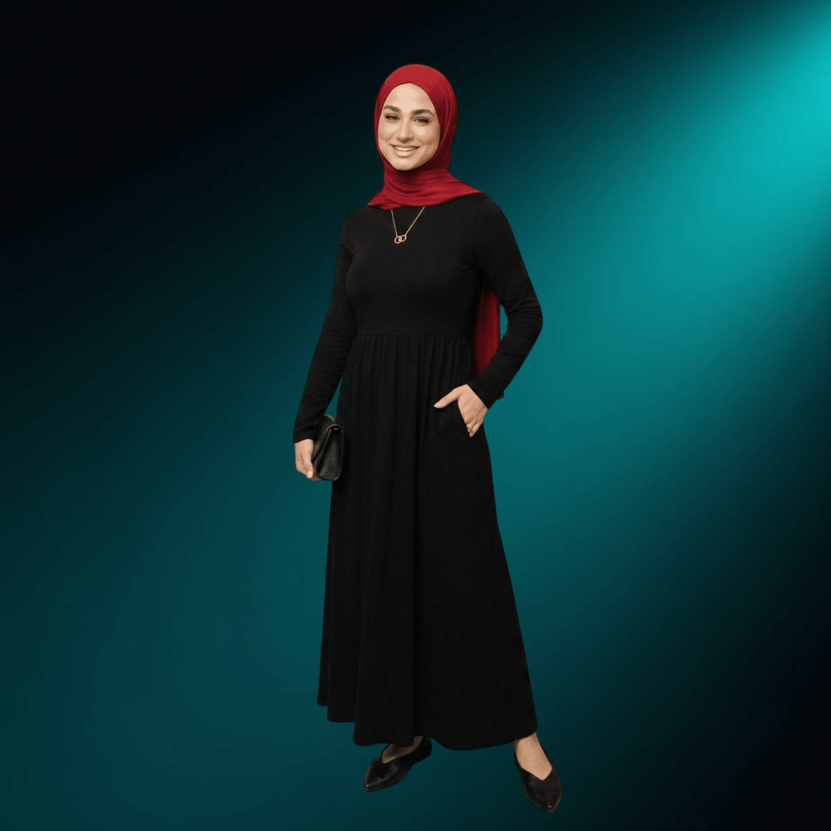 Woman in a red hijab and black dress wearing the NUUR Sanad necklace, full length